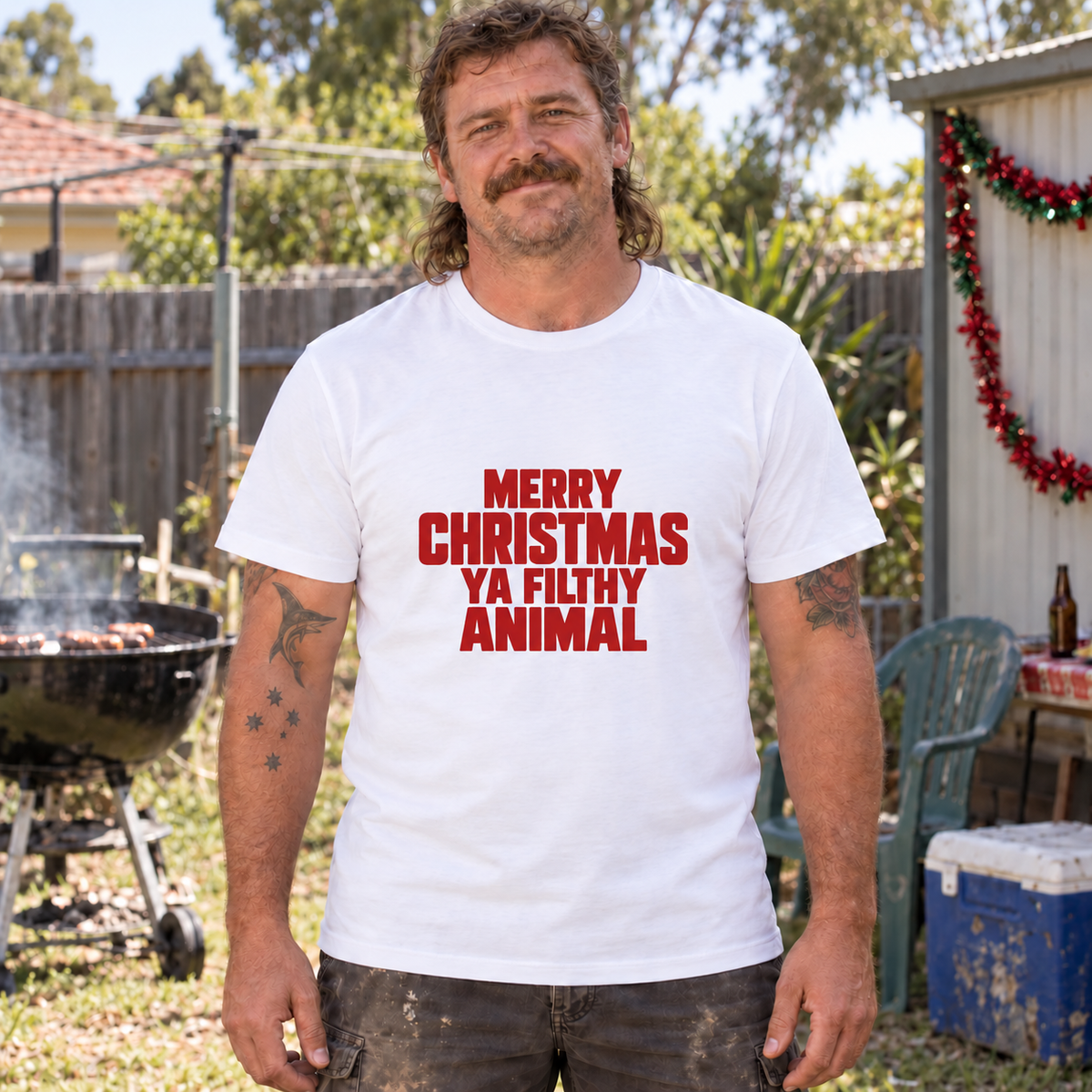 Australian backyard model wearing a white men's Christmas tee with Merry Christmas Ya Filthy Animal in red block lettering.